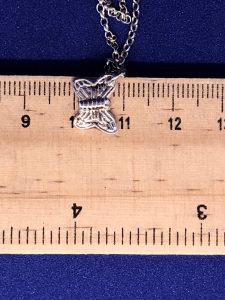 A sterling silver butterfly anklet being measured on a ruler