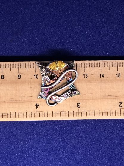 A sterling silver shield necklace being measured on a ruler