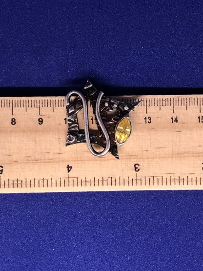 A sterling silver shield necklace being measured on a ruler
