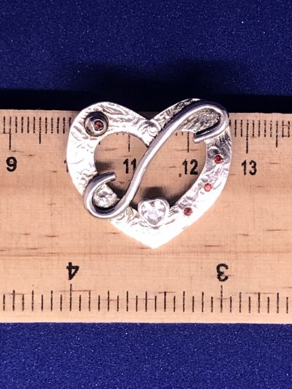 A sterling silver heart necklace being measured on a ruler