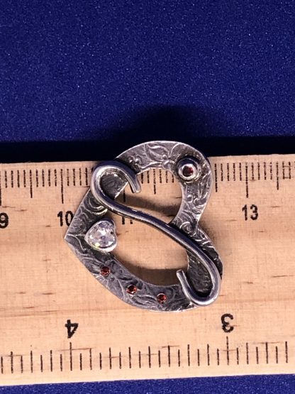 A sterling silver heart necklace being measured on a ruler